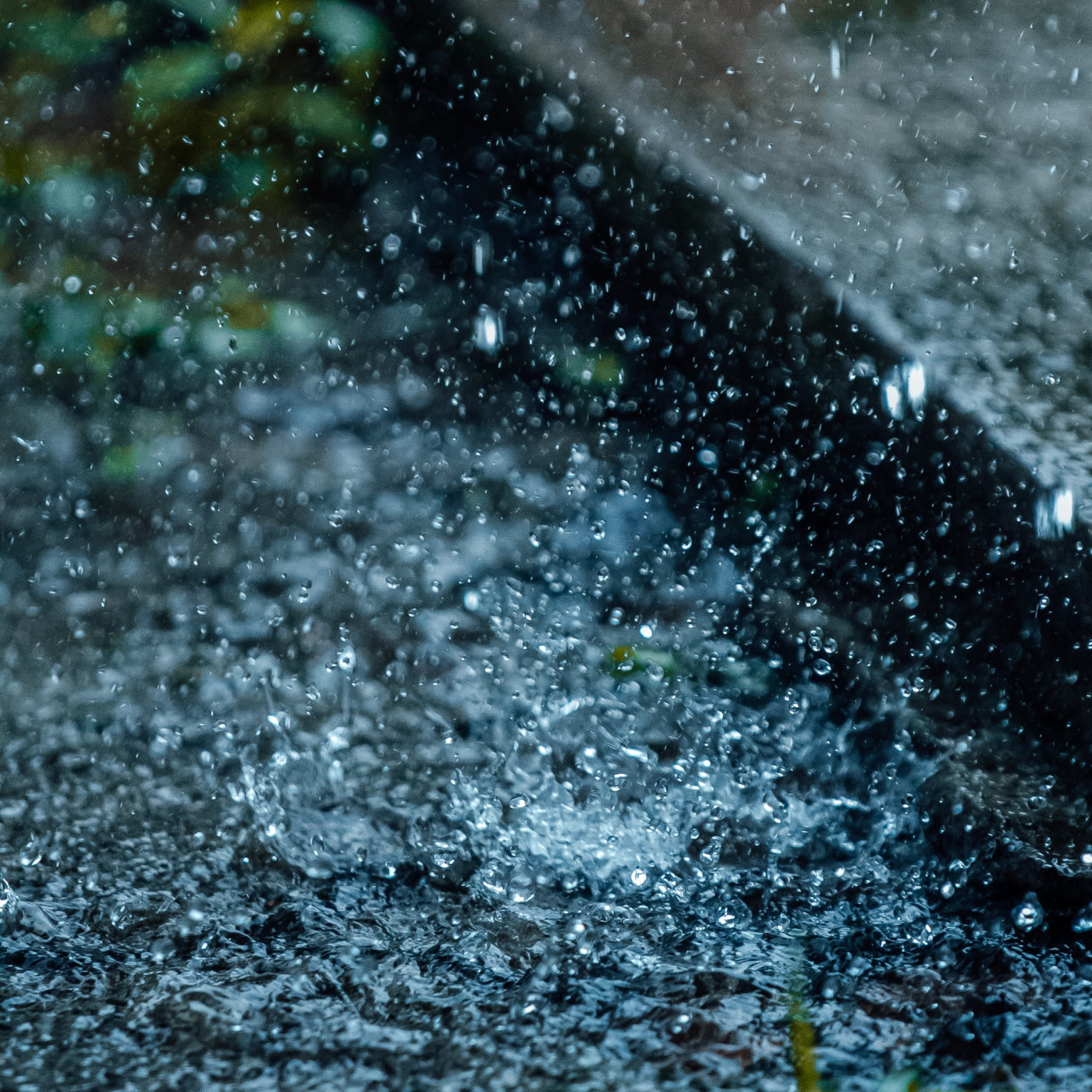 Macro close up shot of rain hitting the ground into a puddle and splashing. The image is blurry with the movement of the heavy rain.